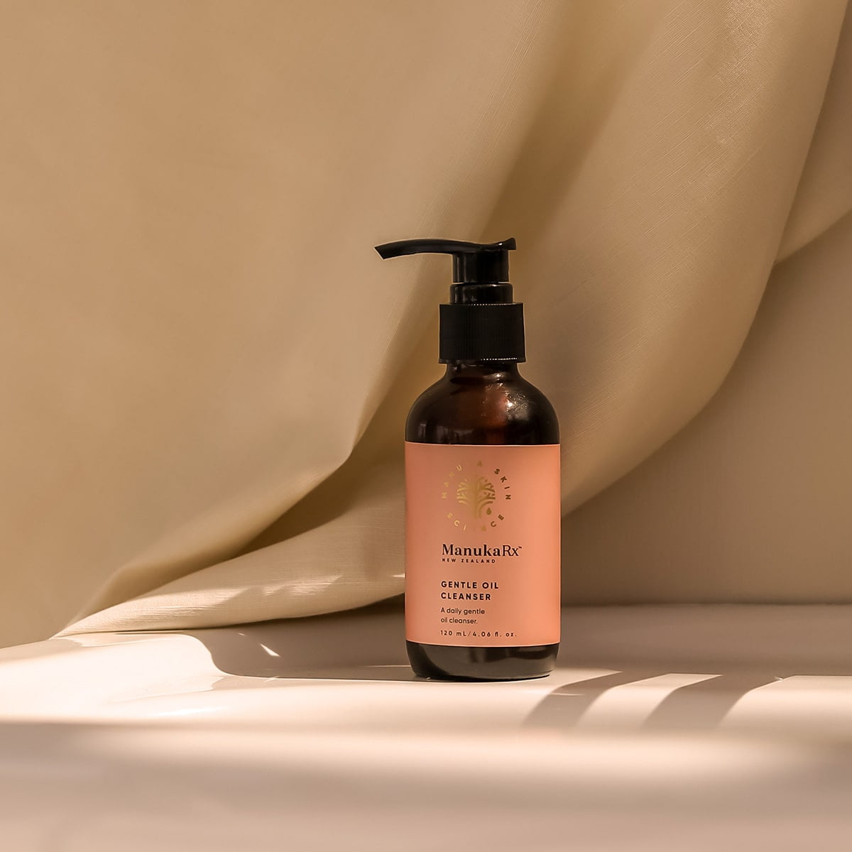 Bottle of ManukaRx Gentle Oil Cleanser with a cream coloured fabric background