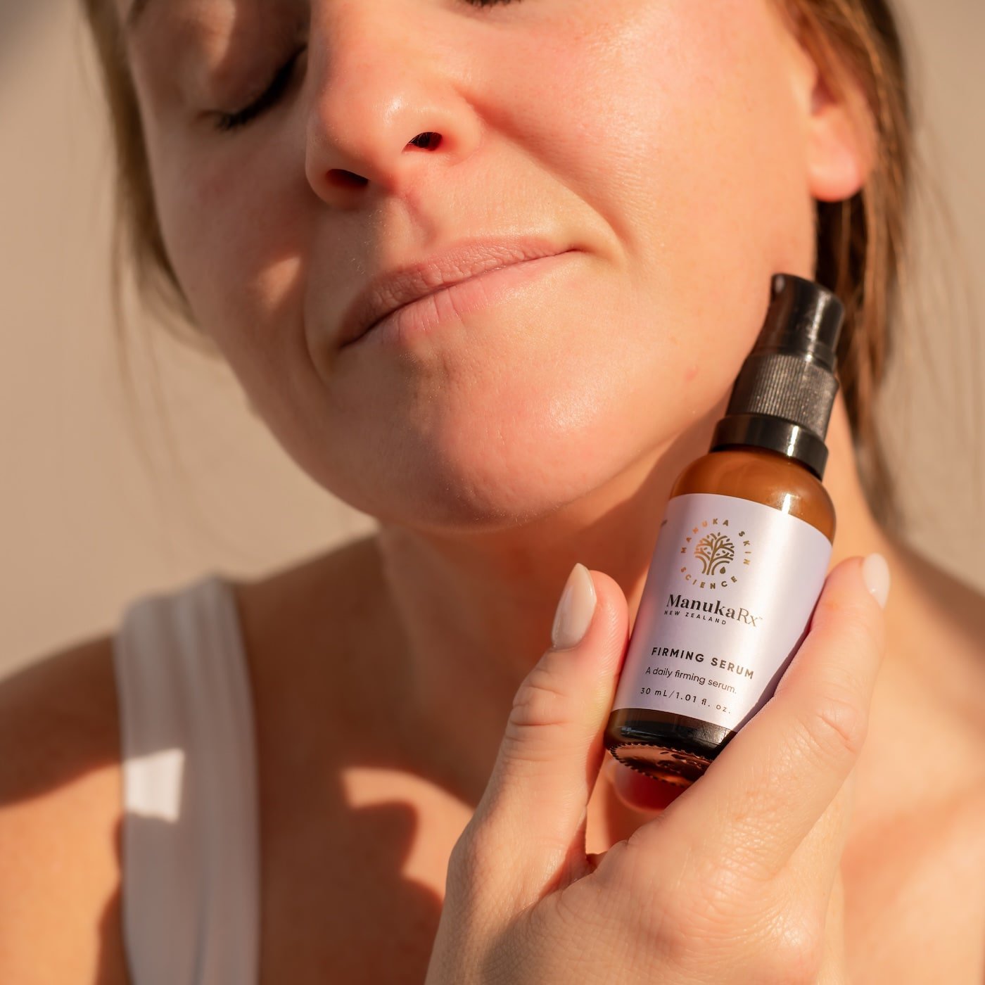 Woman holding bottle of ManukaRx Firming Serum