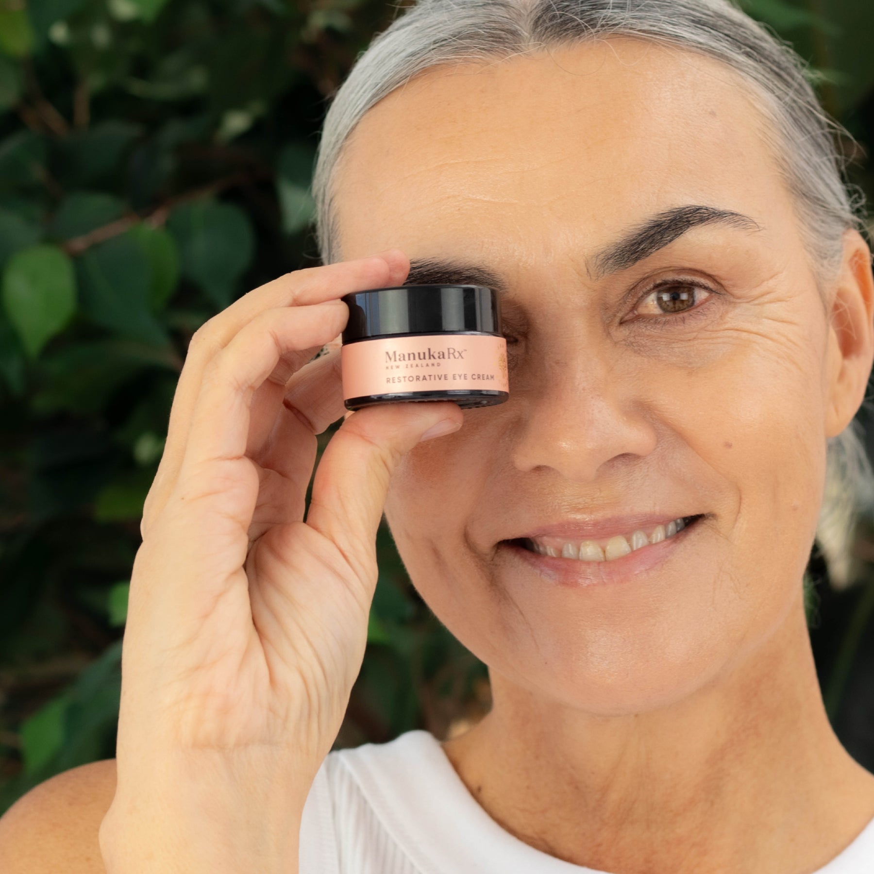 Woman holding jar of ManukaRx Restorative Eye Cream